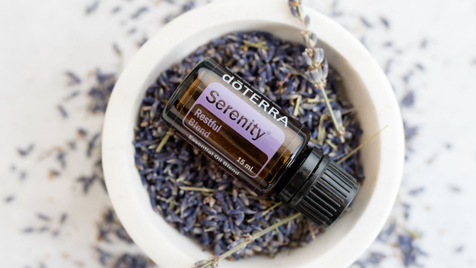 A bottle of doTERRA Serenity Restful Complex oil resting in a bowl filled with fresh sprigs of lavender, creating a calming and soothing visual that highlights the product’s relaxing qualities.