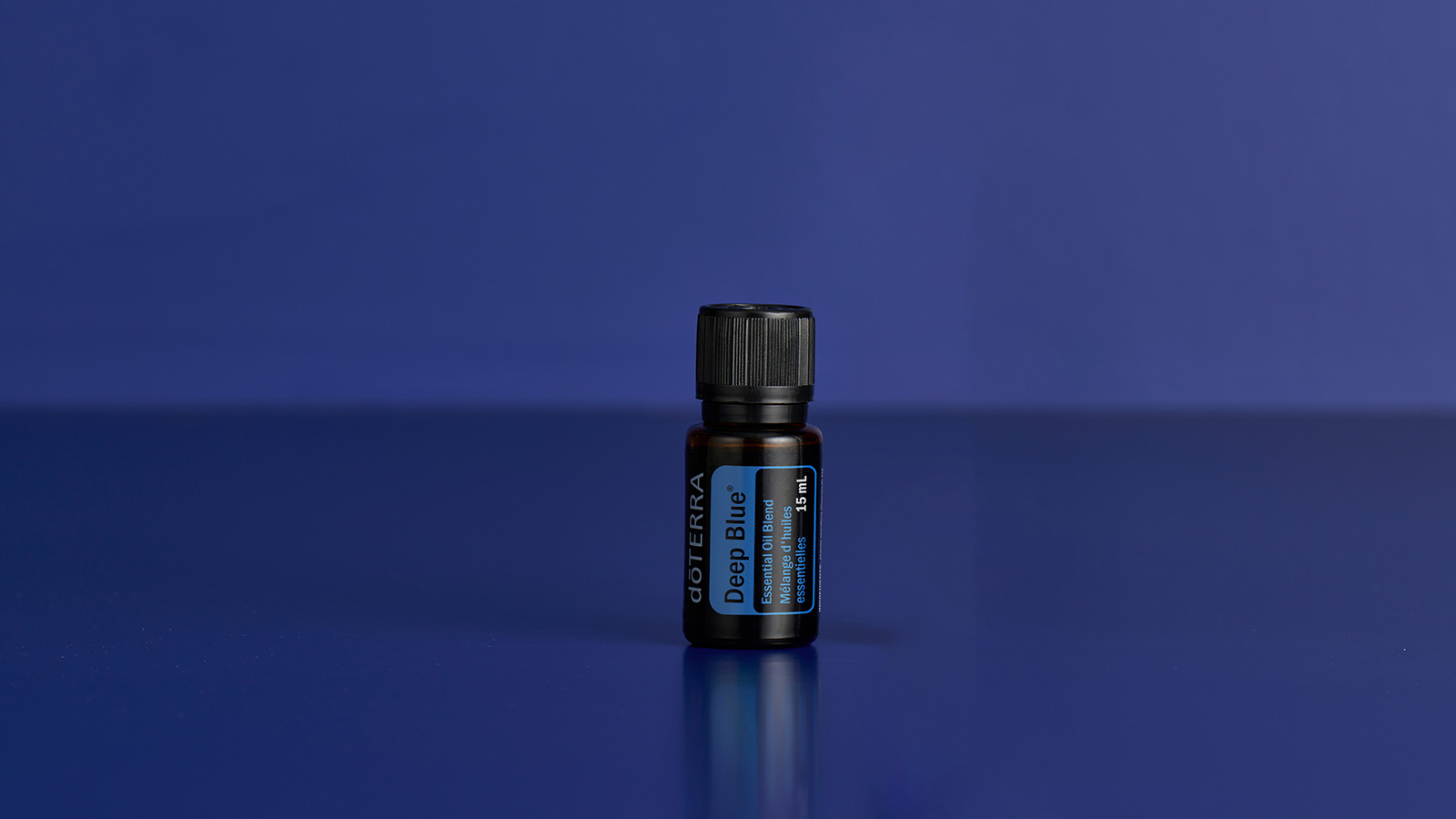 A bottle of doTERRA Deep Blue essential oil displayed upright against a rich deep blue background, emphasizing the product's signature color and soothing identity.