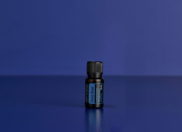 A bottle of doTERRA Deep Blue essential oil displayed upright against a rich deep blue background, emphasizing the product's signature color and soothing identity.