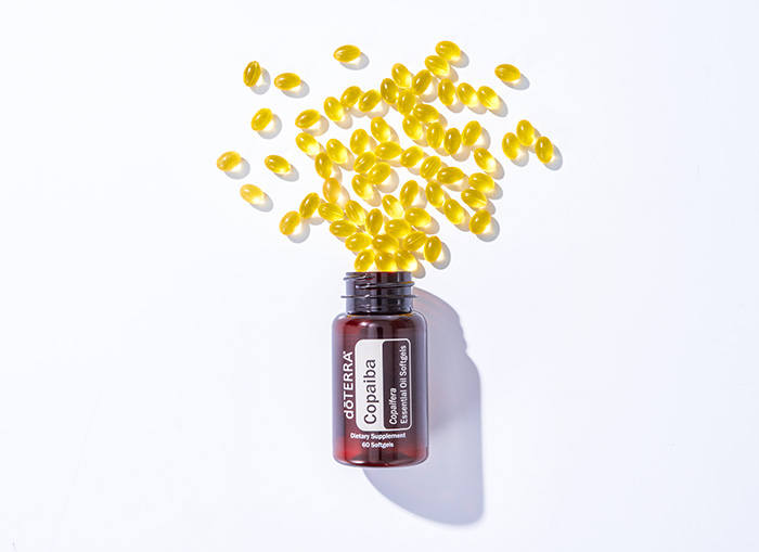 doTERRA Copaiba Softgels sitting on a long, rectangular rock. A few softgels sit to the side of the bottle. 