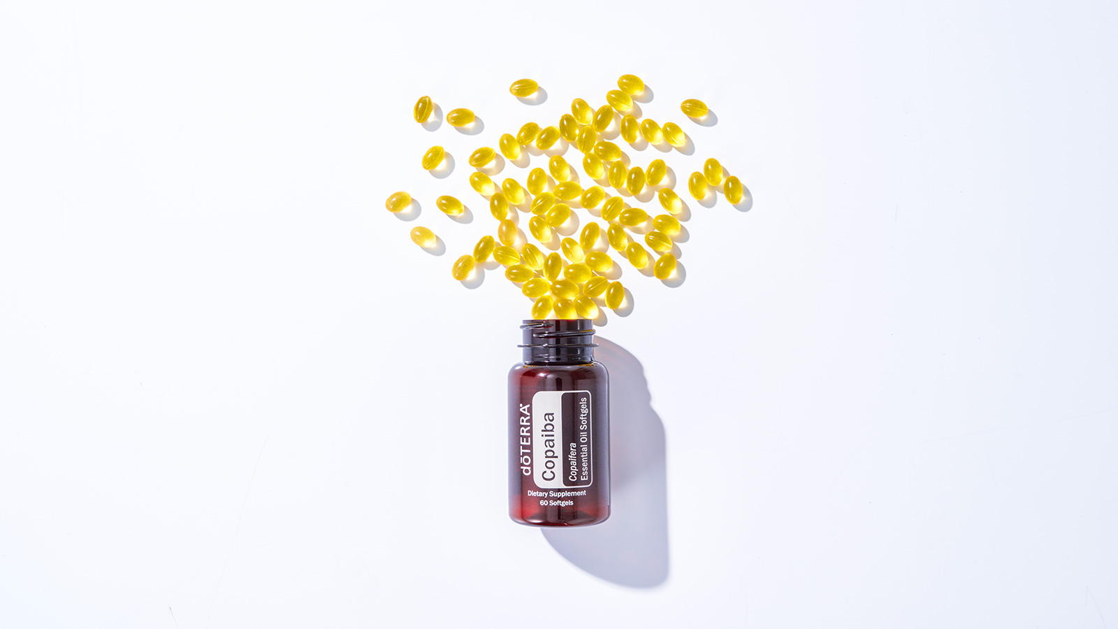 doTERRA Copaiba Softgels sitting on a long, rectangular rock. A few softgels sit to the side of the bottle. 