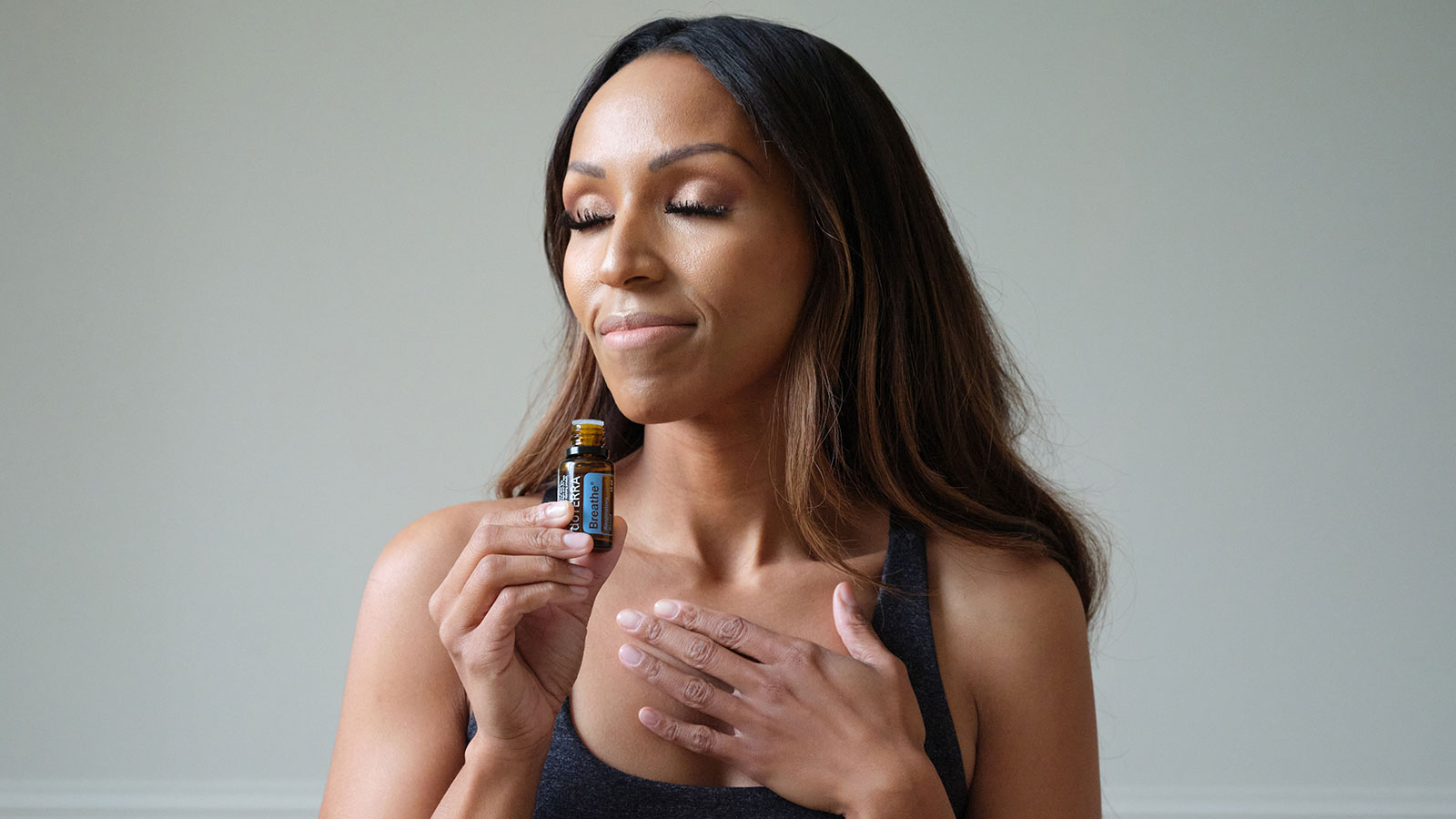 A woman closes her eyes and inhales deeply from a bottle of doTERRA Breathe essential oil. The moment captures a sense of calm and clarity, highlighting the refreshing blend’s ability to promote feelings of open airways and easy breathing.