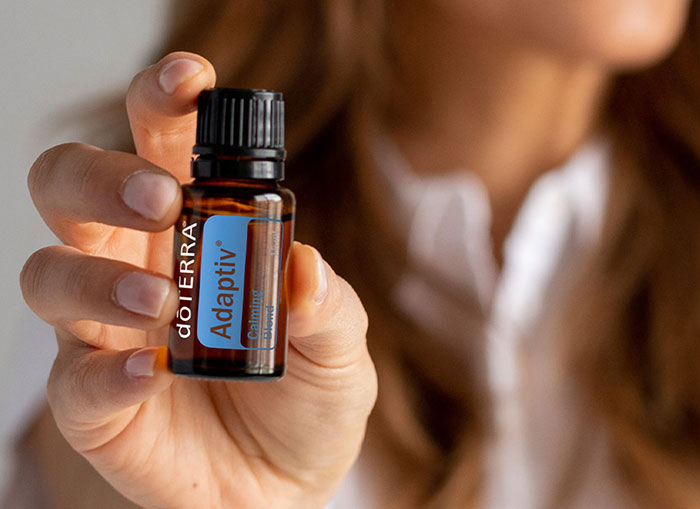 Woman holding a bottle of dōTERRA Adaptiv essential oil, symbolizing calm and balance. 