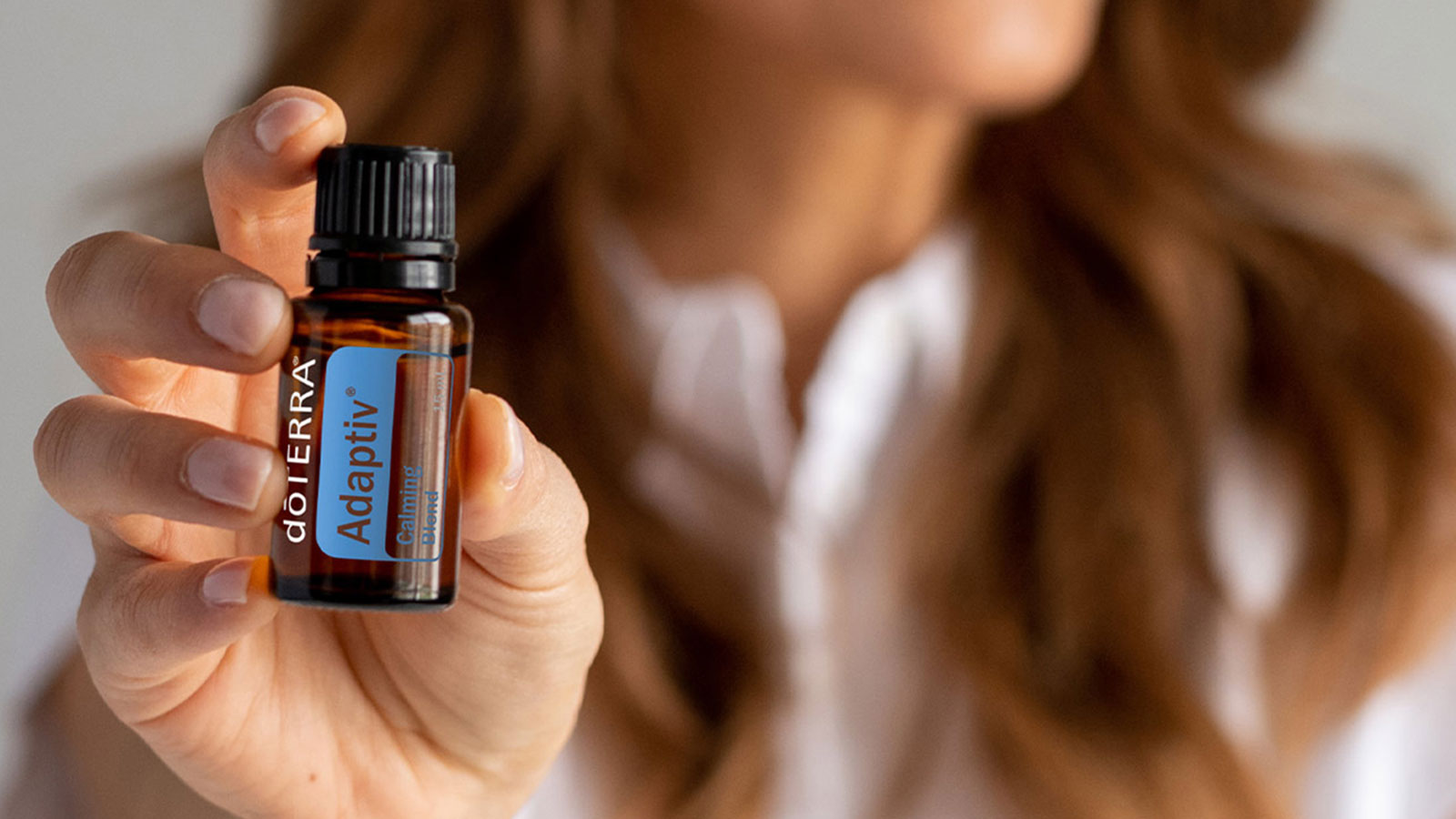 Woman holding a bottle of dōTERRA Adaptiv essential oil, symbolizing calm and balance. 