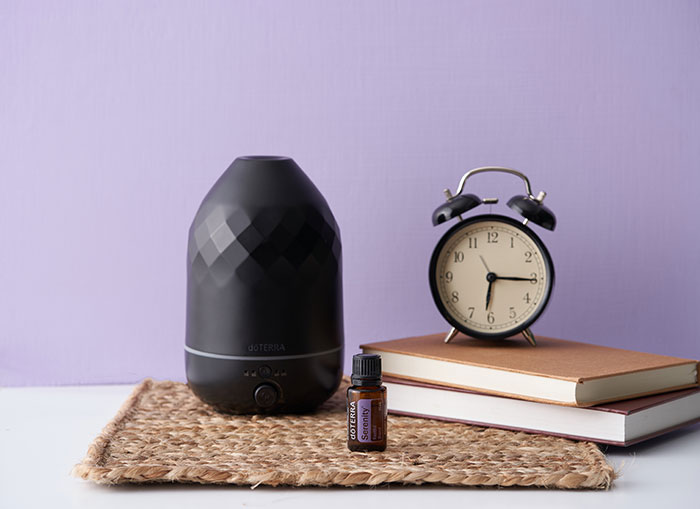 doTERRA Serenity essential oil bottle placed beside a Volo diffuser and an alarm clock, creating a calm, peaceful setting that promotes rest and better sleep.