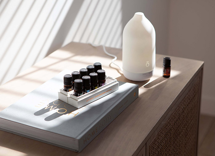 A doTERRA Laluz diffuser sits on a wooden cabinet beside a small bottle of essential oil and a tray of doTERRA oils for a homemade diffuser blend.