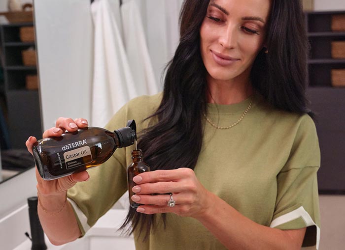 A woman pouring a bottle of castor oil into a glass