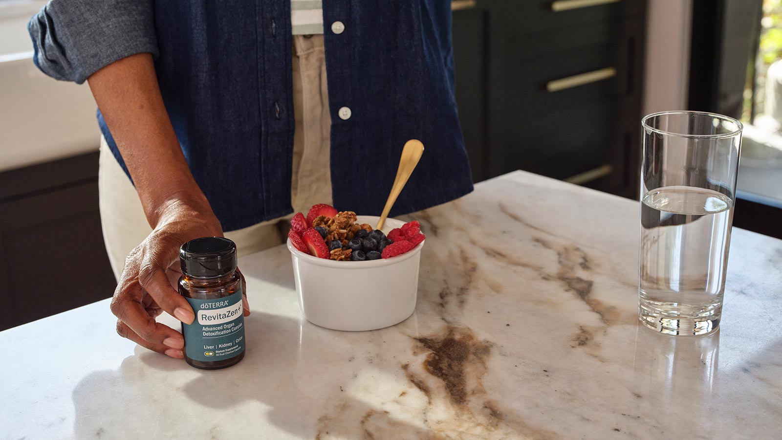 A person standing next to a counter with fruit and RevitaZen+ on it