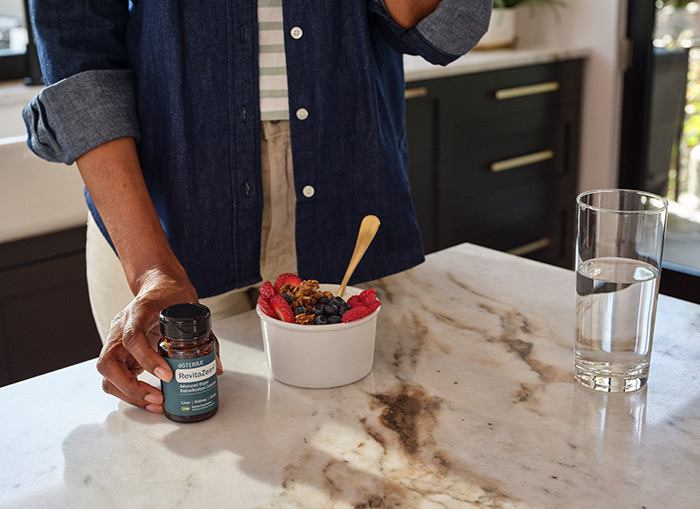 A person standing next to a counter with fruit and RevitaZen+ on it